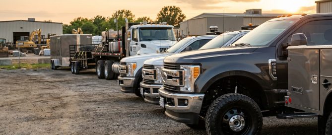 A high-end magazine quality photograph of a commercial fleet parked in a contractor's yard at golden hour, showing clean