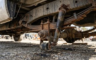 A photorealistic, high-end close-up of worn truck suspension components beneath a heavy-duty commercial pickup truck